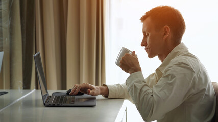 Businessman working on laptop and drinking coffee in hotel room