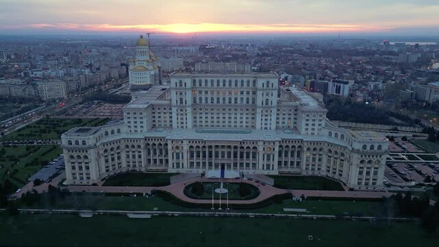 Aerial drone footage of the house of the people in Bucharest. High angle golden hour shot of the  Parliament building in the capital or Romania. Massive governmental structure seen from the air.
