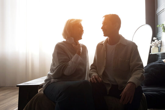 Senior couple sharing intimate moments in bedroom during sunrise - Powered by Adobe