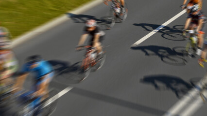 A group of cyclists pedal down a street, their motion blurred in an aerial view. The dynamic scene...