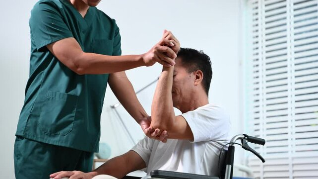 Asian physiotherapist helps senior patient on wheelchair with arm exercises during stroke recovery. Elderly care, rehabilitation