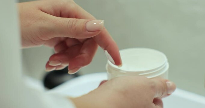 Closeup of woman hold jar with lifting cream in hands and applying on body for smooth healthy skin. Beauty cosmetics at home.