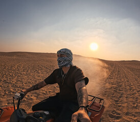 Tourist riding quad bike and taking selfie in desert at sunset