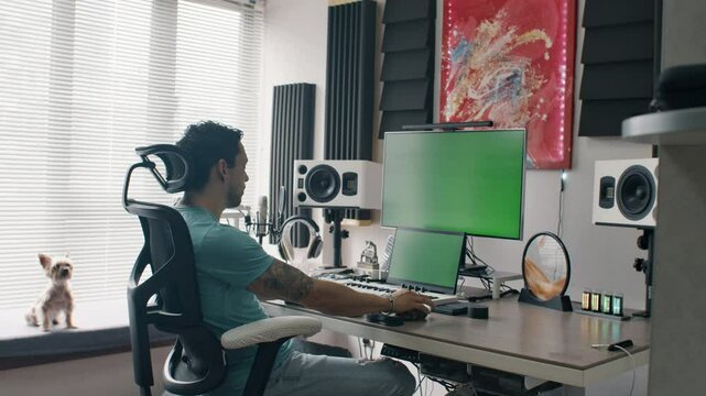 Music producer working at audio workstation in home studio with green screen monitors