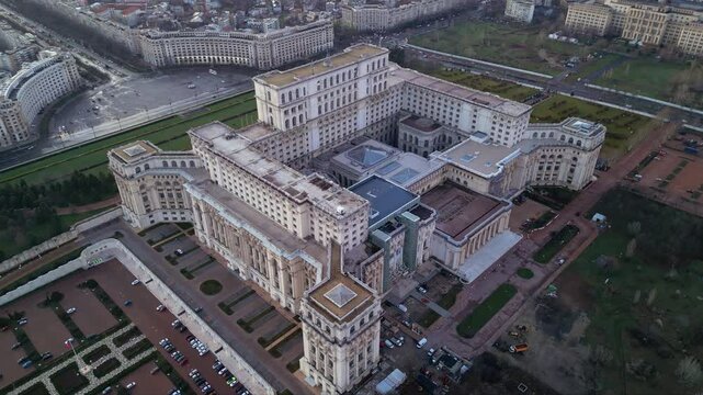 Aerial drone footage of the house of the people in Bucharest. High angle golden hour shot of the  Parliament building in the capital or Romania. Massive governmental structure seen from the air.
