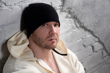 Man in black beanie and fleece hoodie sitting against wall.