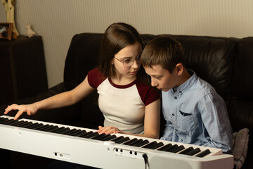 Girl teaching boy to play the keyboard. Practicing piano at home