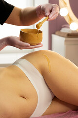 Beautician dripping honey onto thigh during cosmetic body treatment. Honey detox massage or caramel liposuction