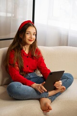 Portrait of smiling teen girl holding tablet on sofa. Concept of lifestyle, use digital technology