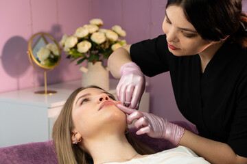 Practitioner performs chin filler injection on reclining client in studio. Aesthetic cosmetology. Lip Augmentation. Female client during procedure in beauty clinic