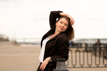 Woman in brown suit resting arm on railing, looking to side outdoors. Natural feel with soft light. Casual, confident pose and expression add genuine and approachable vibe.