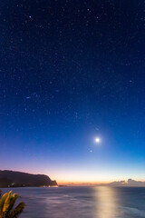 Long exposure scenic view of North Shore of Hawaiian island of Kauai with its famous Napali coast at night against blue sky with moon and stars