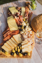Catering on a wooden board on a rustic table, meat, olives, cheese, and a drink as an appetizer