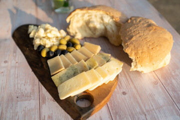 Tasty cheese and olives on a wooden board and homemade bread on the table on a sunny day in golden hour