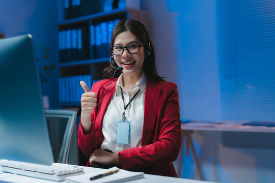 Asian businesswoman showing thumbs up working overtime in office at night