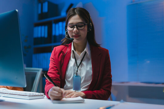 Asian operator working night shift taking notes in notebook while talking on headset