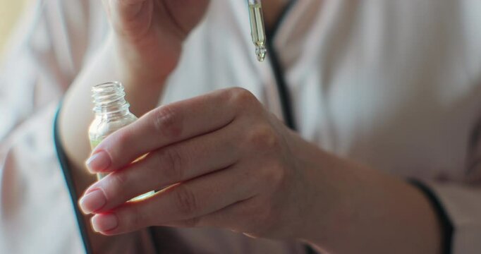 Woman dropping moisturizer with pipette in hand. Young woman applying rejuvenating serum on her hand and body.