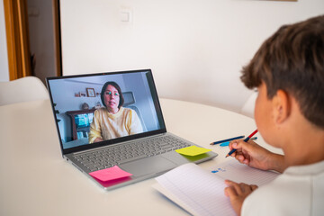 A child participates in an online tutoring session, intently focused on a teacher visible on the laptop screen.