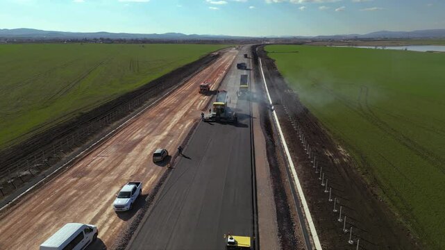 Drone aerial view of construction truck driving on partially built road. Highway infrastructure project with earthworks, soil compaction and gravel transport for modern civil engineering and developme