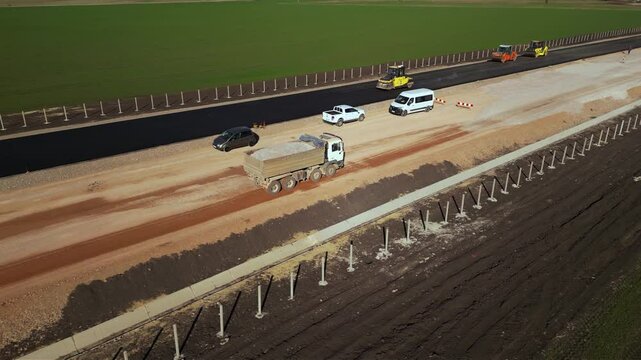 Drone aerial view of construction truck driving on partially built road. Highway infrastructure project with earthworks, soil compaction and gravel transport for modern civil engineering and developme