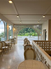 Editorial image. Restaurant Terrace with Mountain View. Elegant restaurant terrace featuring wicker dining chairs and decorative geometric screens with scenic mountain lan. Krabi, Thailand. April 2025