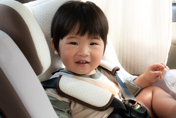 happy Asian baby or toddler sitting and playing bottle in car seat, safety chair between travelling