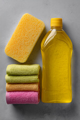 dishwashing liquid in yellow bottle, sponge and napkins of different colors on gray surface
