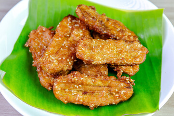 Crispy Thai fried bananas with sesame seeds served on a banana leaf in a white plate, Fried bananas is a traditional Asian snack with sweet, crunchy texture. Top view close-up shot