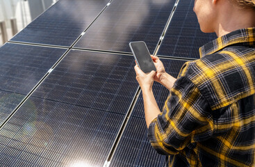 Female maintenance worker checking solar panel performance on smartphone