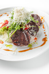 Gourmet dish with seared beef medallions, shredded cheese, fresh greens, and sliced tomatoes, drizzled with orange sauce on a white plate, presented elegantly for fine dining.