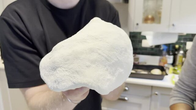 Closeup slow shot of hands stretching and rotating a piece of flat dough, to form a pizza base.