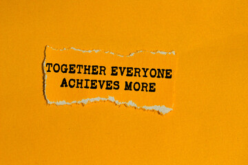 Together everyone achieves more message written on ripped torn orange paper piece on orange background. Conceptual together everyone achieves more symbol. Copy space.