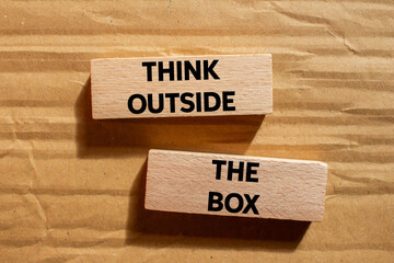 Think outside the box message written on wooden blocks on cardboard background. Conceptual think outside the box symbol. Copy space.