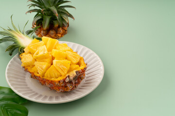 Fresh pineapple chunks served in a pineapple bowl on green table background.