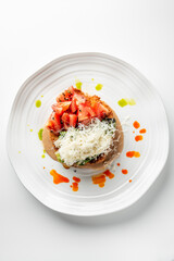 A plate of meat topped with fresh diced tomatoes, grated cheese, and aromatic herbs, elegantly presented with colorful sauce drizzles, highlighting a gourmet culinary experience
