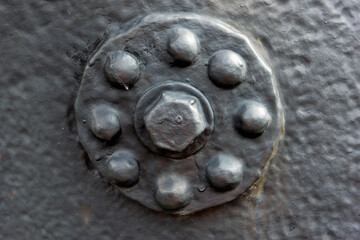 Textured metal bolt with rivets stands out against a dark industrial surface, illuminated by natural light, showcasing its design and structure.