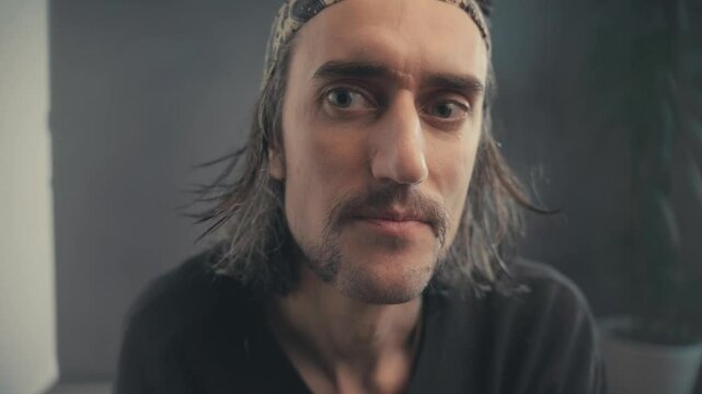 Introspective Portrait of a Long-Haired Man with Patterned Headband: Capturing Emotional Shifts and Intense Gaze in a Muted Setting for a Thoughtful and Engaging Visual Experience