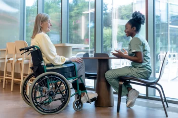 Gordijnen Doctor and patient on a wheelchair talking and looking peaceful © zinkevych