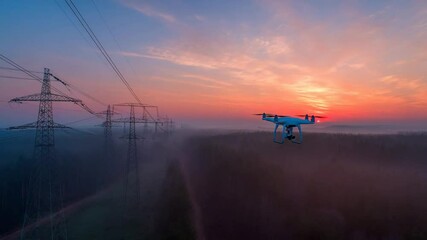 A drone flies near power lines during a beautiful sunset, with a vibrant sky above a misty forest.