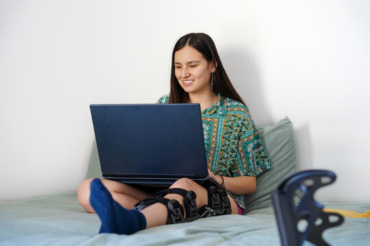 Teen girl with broken leg using laptop while resting at home