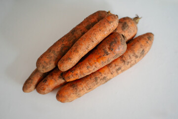 Bright orange ripe carrots with dirt from the ground in a bed on a white surface, emphasizing their freshness and natural beauty. Healthy vegetables look attractive.