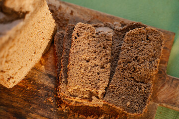 Homemade black dark Darnitsky rye bread with sun light on a wooden board on a green napkin close-up. A lots of fresh bread crumbs on the board, it looks very appetizing, invites to a healthy snack.