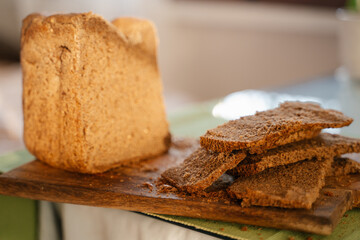 Homemade black dark Darnitsky rye bread with sun light on a wooden board on a green napkin close-up. A lots of fresh bread crumbs on the board, it looks very appetizing, invites to a healthy snack.