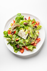 A fresh Greek salad with feta cheese, olives, tomatoes, cucumbers, and mixed greens, garnished with herbs on a white plate. The vibrant colors and healthy ingredients create an appetizing Mediterranea