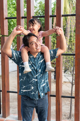 Obraz premium Hispanic father carrying daughter on shoulders, enjoying family time outdoors
