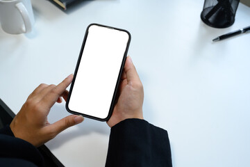 A person is holding a cell phone with a white screen. The phone is on a table with a pen and a cup
