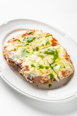 Rectangular pizza with melted cheese and green pesto sauce on a white oval plate. Cut into four pieces, it has a crispy crust and vibrant colors, making it look fresh and appetizing.