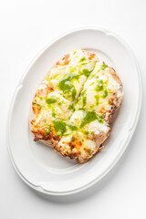 Rectangular pizza with melted cheese and green pesto sauce on a white oval plate. Cut into four pieces, it has a crispy crust and vibrant colors, making it look fresh and appetizing.