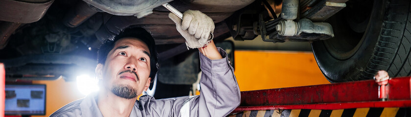 Automobile technician inspecting the underside of a lifted vehicle in a service garage, demonstrating hands-on diagnostics, maintenance, and professional car repair in a mechanical workshop.