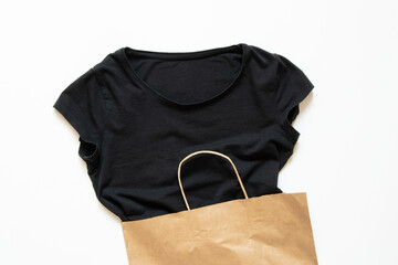 Black T-shirt half in a paper kraft bag on a white background, clothes shopping, shopping, delivery...